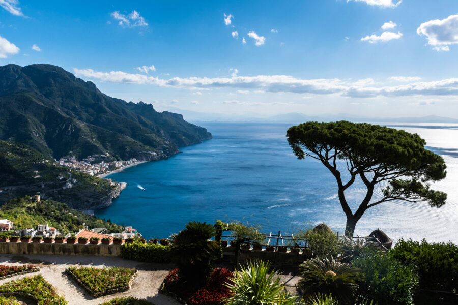 A stunning coastal garden vista with ocean, mountains, flowers, and serene sky.