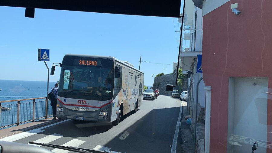 Amalfi SITA bus drives down a narrow street, with a car following closely behind it.