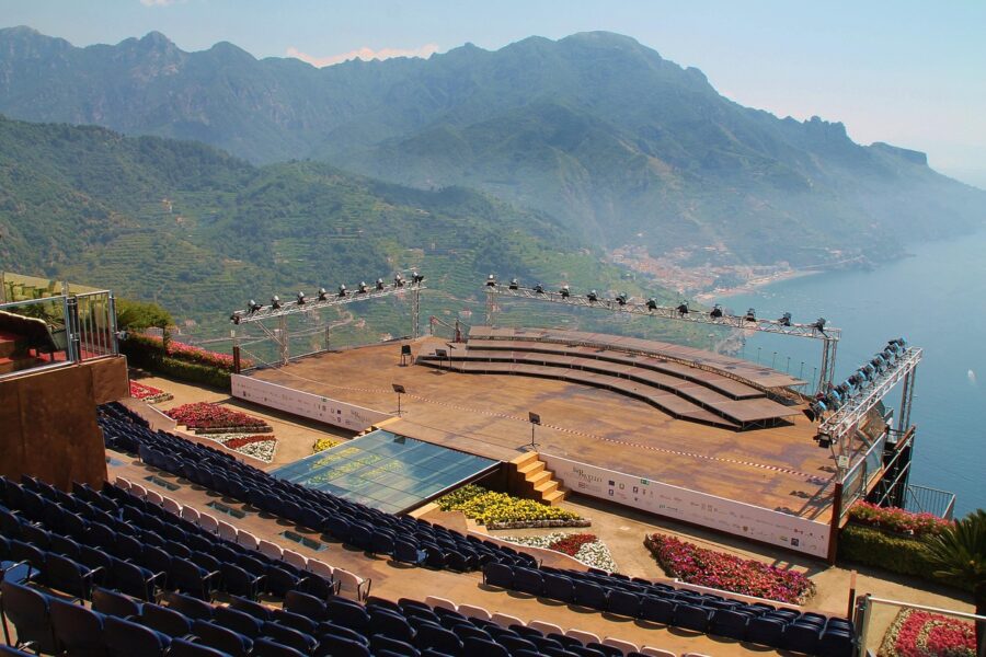 Outdoor amphitheater with mountain and sea views, featuring blue seating and flower beds.