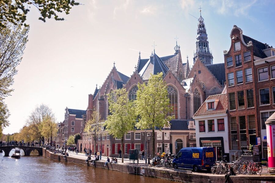 Amsterdam canal scene with traditional houses, church spires, bicycles, and lush greenery.