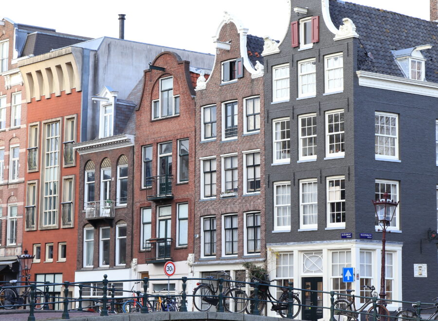 Colorful canal house facades in Amsterdam's Jordaan District, with a bridge and bicycles parked nearby.