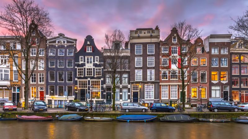 Amsterdam canal at sunset with iconic Dutch townhouses and boats reflecting vibrant urban life.