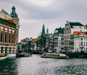 Amsterdam canal scene with historic architecture, boats, and overcast sky.