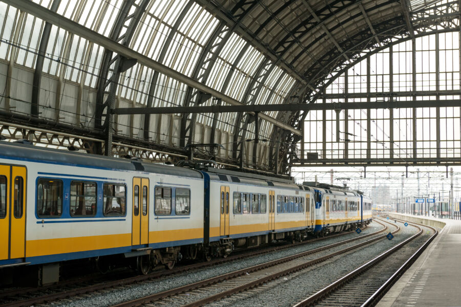 Amsterdam Centraal Station filled with NS trains and trams, surrounded by a vibrant crowd along the IJ river.