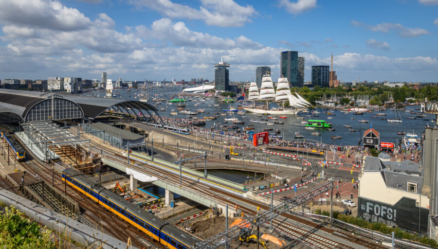 Aerial view of Amsterdam Central Station showcasing NS trains and trams amidst the vibrant cityscape.