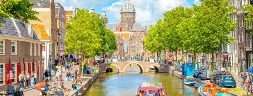 Scenic view of Amsterdam's De Wallen district, featuring a canal surrounded by traditional architecture and lively streets.