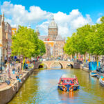 Scenic view of Amsterdam's De Wallen district, featuring a canal surrounded by traditional architecture and lively streets.
