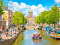 Scenic view of Amsterdam's De Wallen district, featuring a canal surrounded by traditional architecture and lively streets.
