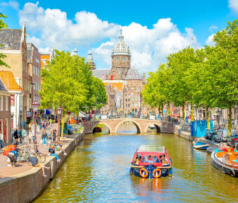 Scenic view of Amsterdam's De Wallen district, featuring a canal surrounded by traditional architecture and lively streets.