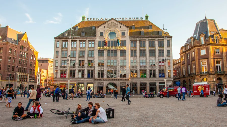 Amsterdam Dam Square with Madame Tussauds museum, historic buildings, tourists, bicycles, and street vendors.