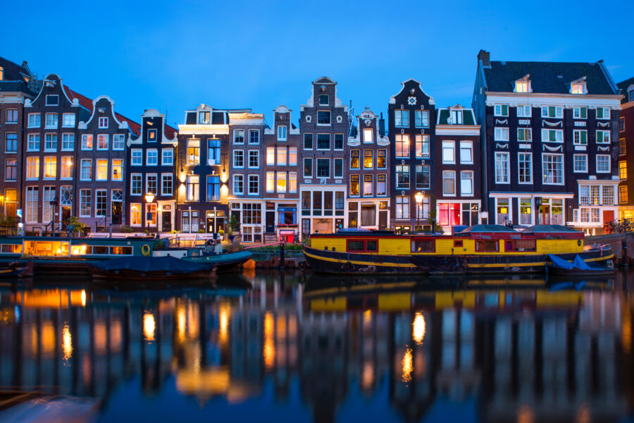Nighttime scene of an Amsterdam canal, showcasing typical Dutch architecture and houseboats, illuminated by water reflections