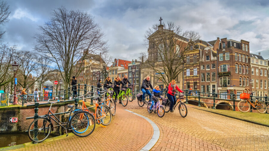 Group of people cycling on a path in Amsterdam's historic center, with a bright winter sun illuminating the scene.