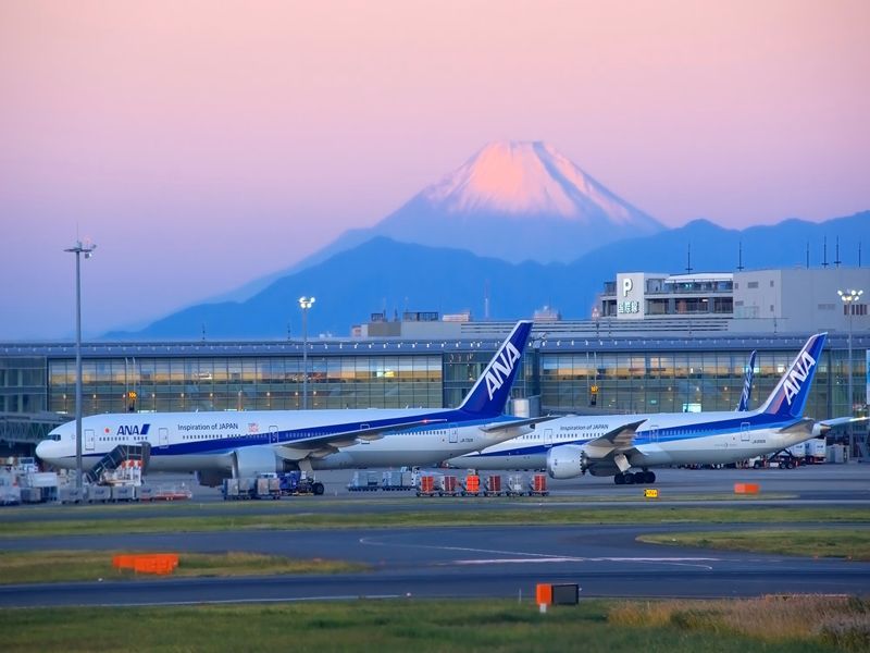 ANA airplanes on tarmac, snowy mountain backdrop, modern airport terminal at sunrise.