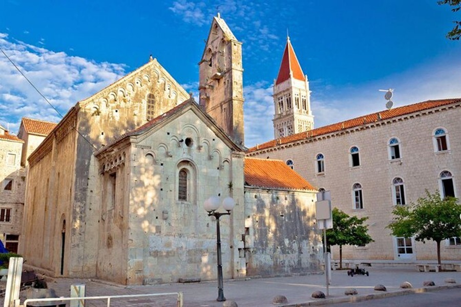 Historic church blending medieval and contemporary styles with Romanesque architecture, bell tower, greenery.