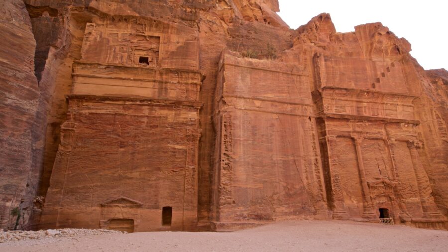 Ancient rock-cut sandstone facades carved into towering cliff, historic archaeological site in desert landscape.