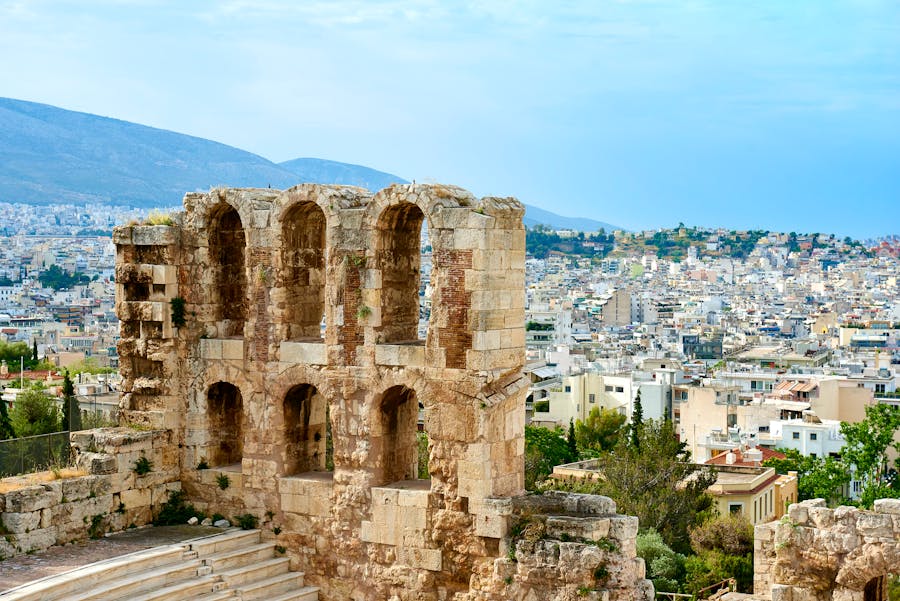 Ancient Roman amphitheater ruins overlooking Athens cityscape and rolling hills.