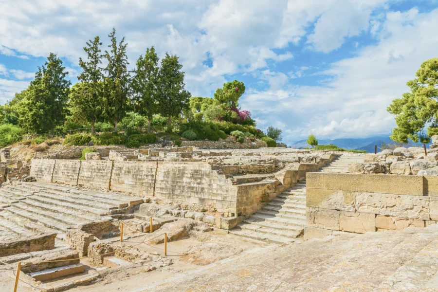 Ancient Phaistos Palace ruins amid lush greenery, vibrant flowers, and clear blue sky.