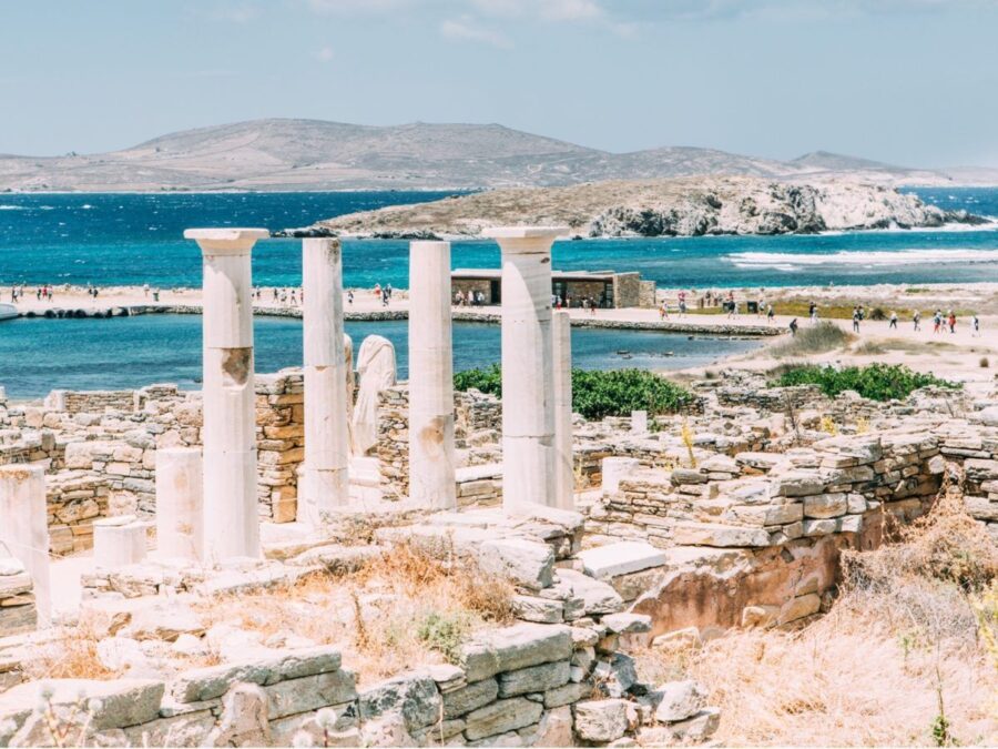Ancient stone columns and Mediterranean sea view at Delos ruins attract tourists.