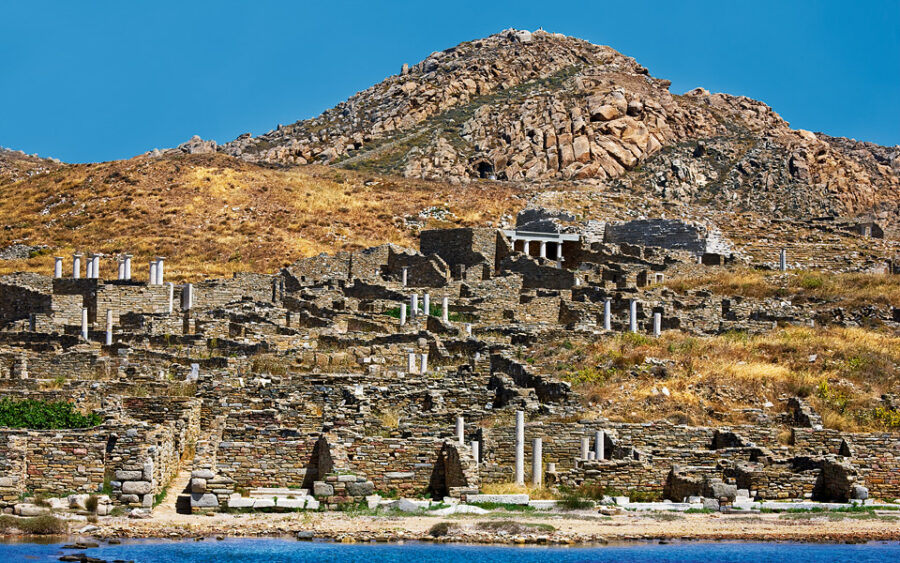 Ancient stone ruins on a rocky hillside with blue sky and reflecting water.