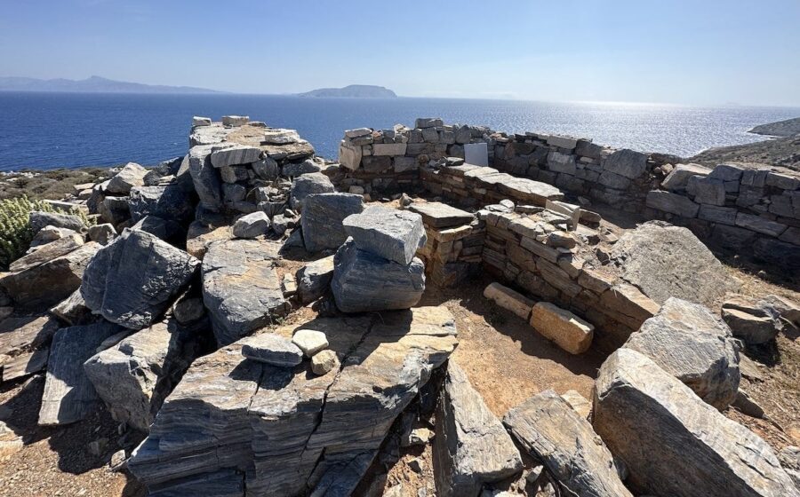 Ancient stone ruins on hilltop overlooking tranquil sea, suggesting historical Greek site.