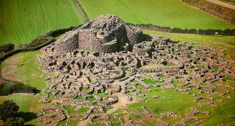 Ancient stone ruins of Nuraghe Su Nuraxi amid lush greenery and rolling hills.