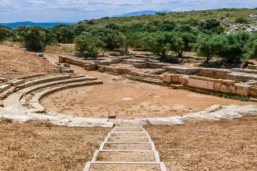 Ancient amphitheater with tiered seating, olive trees, and scenic landscape under a clear sky.