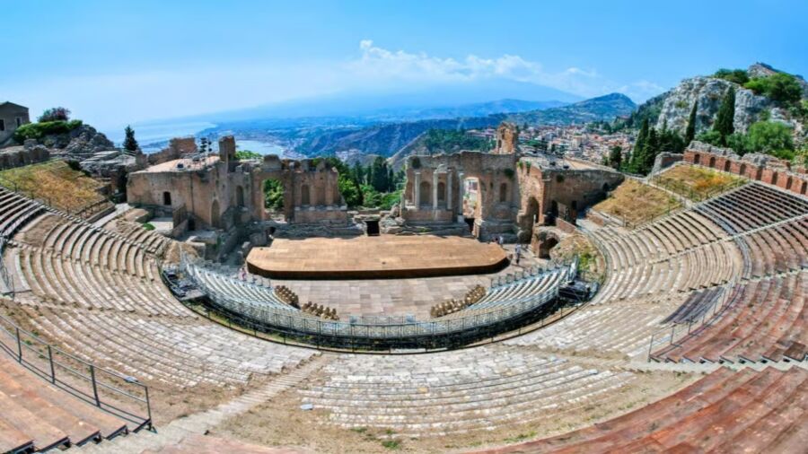 Panoramic view of Taormina showcasing a town with a steeple, highlighting the ancient theatre's historical significance.