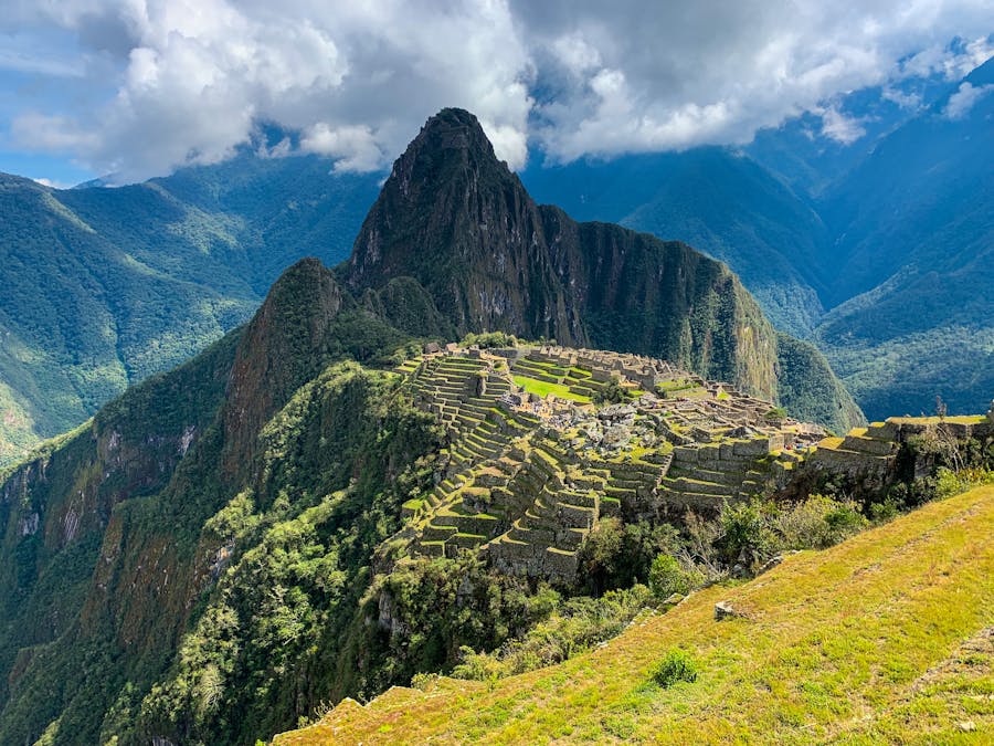 Ancient Andean mountain ruins with terraced fields in lush green valley under dramatic cloudy sky.