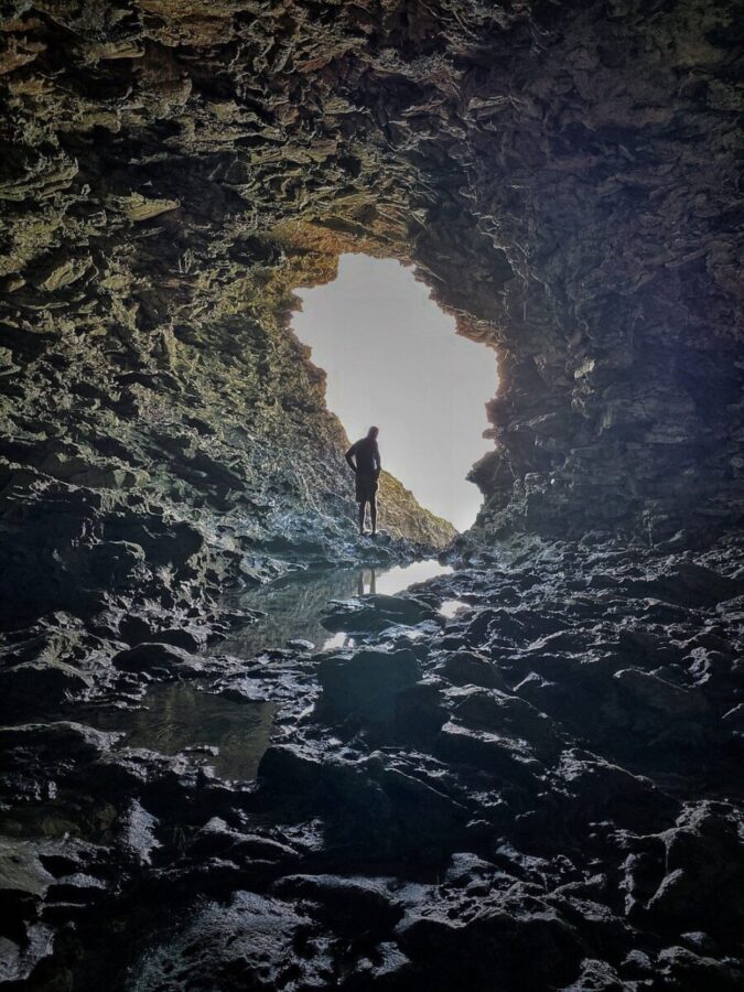 Sunlight filters through the opening of Animal Flower Cave, illuminating a person standing inside the cave in Barbados.