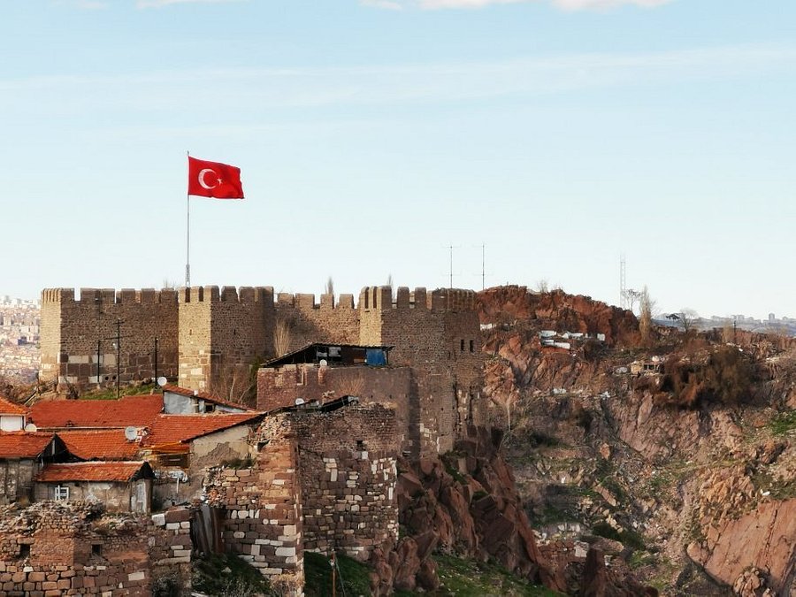 Turkish flag waving above Ankara Castle, with a clear blue sky in the background, showcasing a historic landmark in Istanbul.