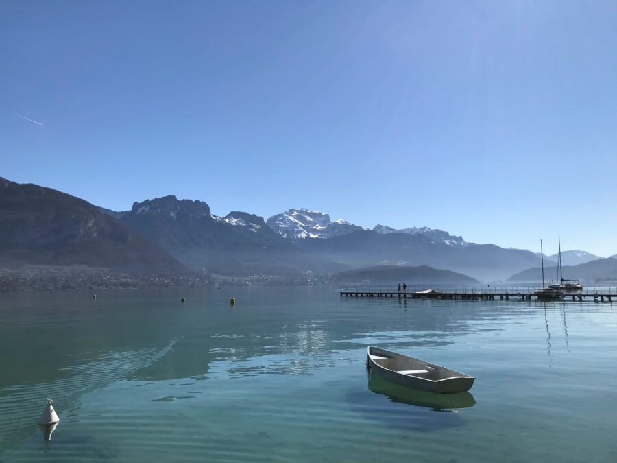 Scenic view of Annecy Lake in France, featuring clear blue waters and lush green shores under a bright sky.