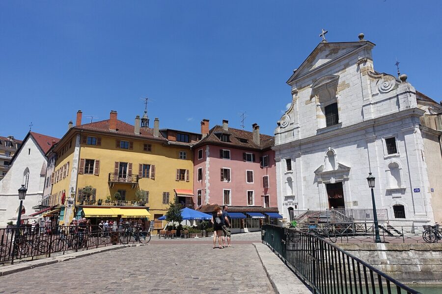 Historic church and adjacent building with clock towers in Annecy Old Town, France, highlighting the area's architectural beauty.