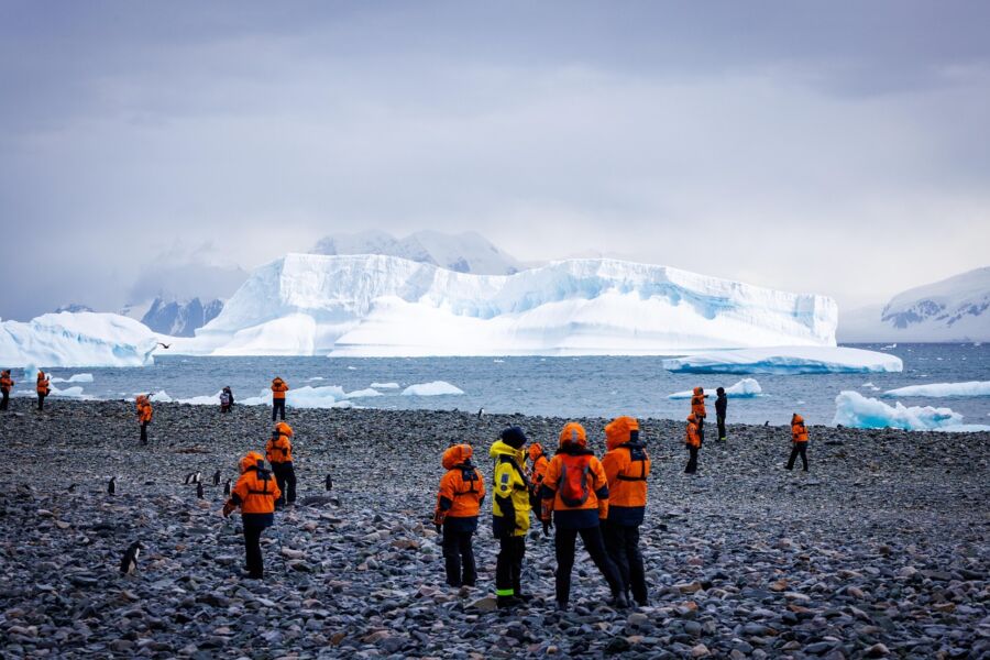 Polar exploration with orange-clad individuals, icebergs, and penguins in an icy landscape.