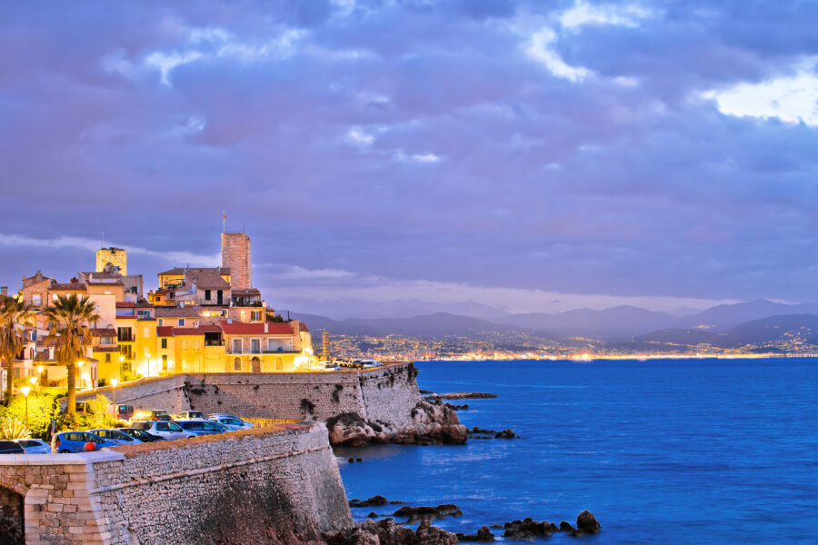 Dawn view of Antibes' historic old town along the seafront, showcasing landmarks bathed in soft morning light.