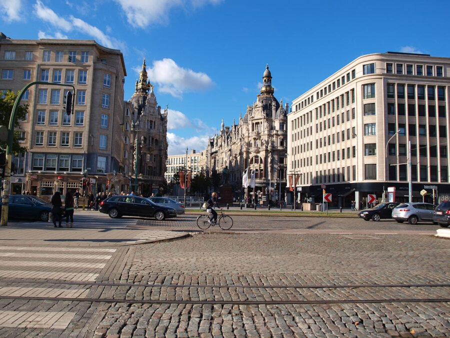 Man rides a bike along a cobblestone street in the Antwerp Diamond District, surrounded by historic buildings.
