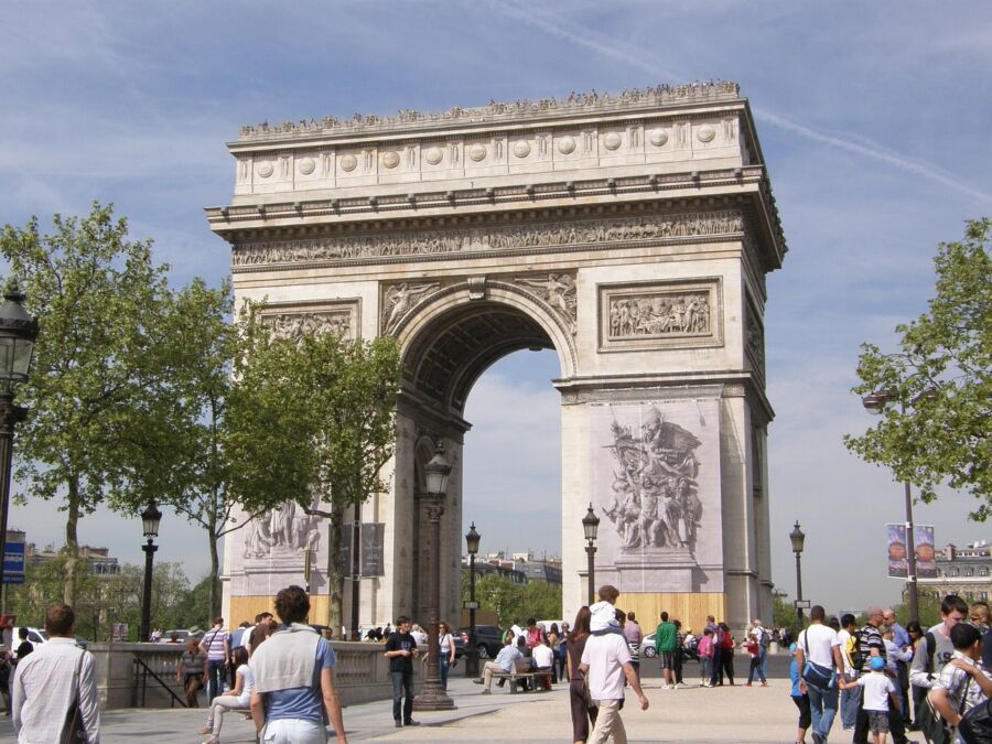Iconic Arc de Triomphe in Paris with tourists and lush trees on a sunny day.