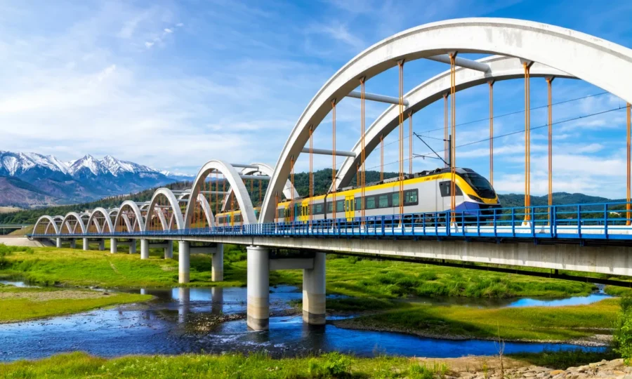 Yellow train on arched railway bridge over river toward Zakopane mountains, Poland.