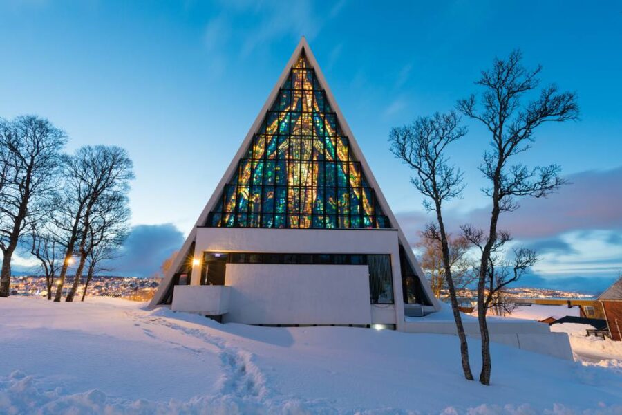 Triangular modern church with glass facade in snowy landscape, surrounded by leafless trees.