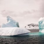 Icebergs floating in serene polar ocean under overcast sky with rugged textures and calm waters.