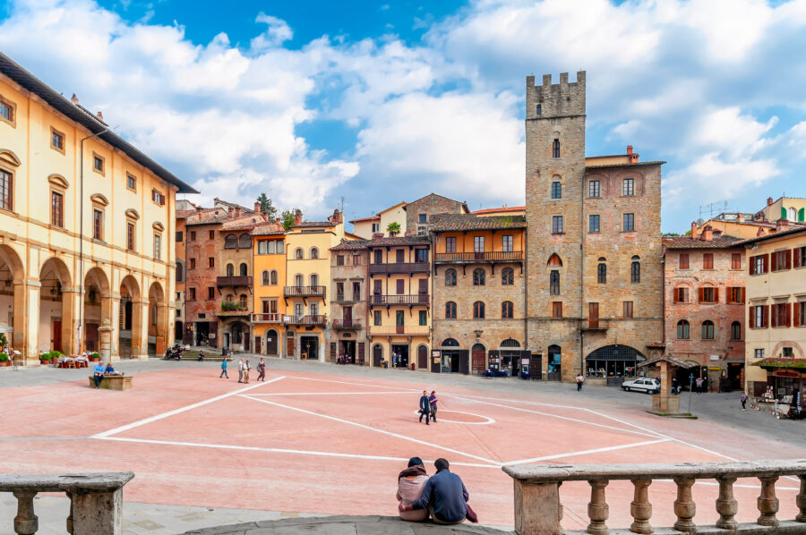 Couple sitting on the ground in Piazza Grande, Arezzo, Italy, surrounded by historic architecture and vibrant atmosphere