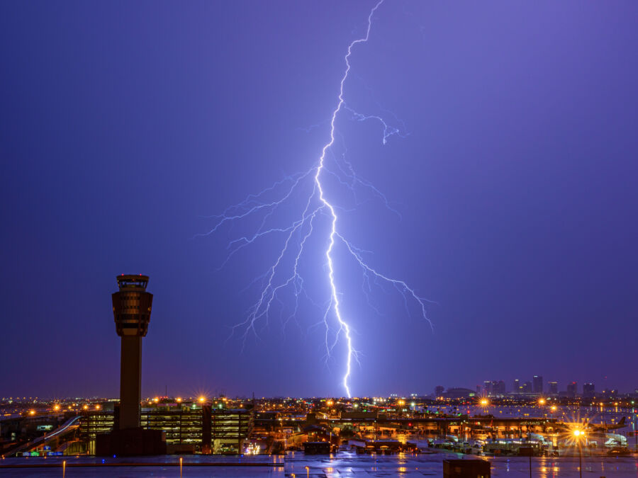 Lightning bolts flash over the Phoenix skyline and airport, creating a striking contrast against the evening sky