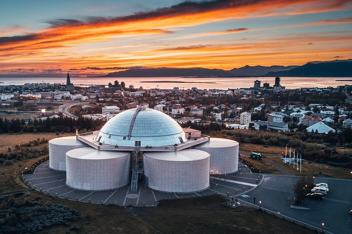 The sun sets over Reykjavik, Iceland, with vibrant colors illuminating the sky, promoting the Áróra planetarium show.