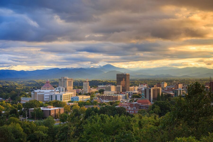 Asheville, North Carolina skyline with tall buildings and majestic mountains in the background under a clear blue sky.