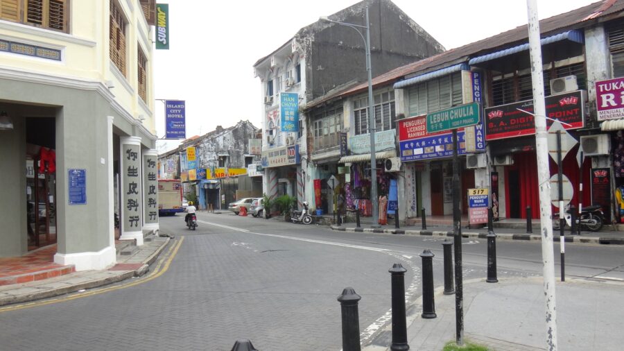 Quiet Southeast Asian old town street with colorful shophouses, hotel signs, motorbike and empty road.