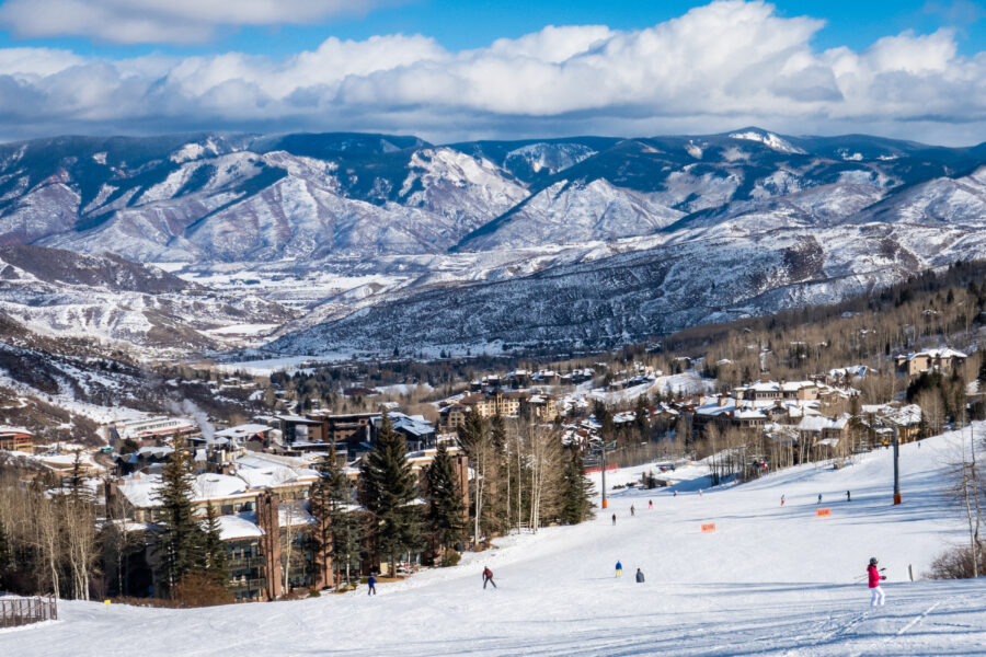 Panoramic view of Snowmass Village with skiers at Aspen Snowmass ski resort and the Rocky Mountains in the background