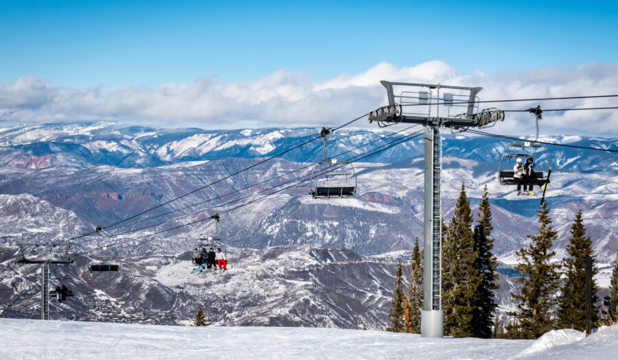 Skiers and snowboarders ride the Elk Camp chairlift at Aspen Snowmass ski resort on a partly cloudy winter day in Colorado