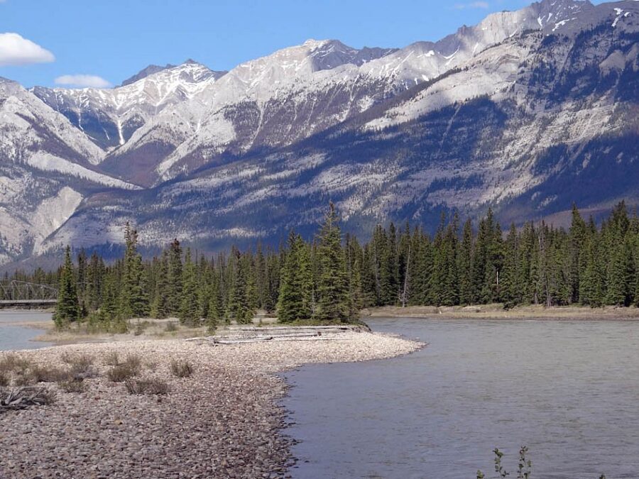 Scenic view of the Athabasca River in Jasper National Park, framed by towering mountains in the distance.
