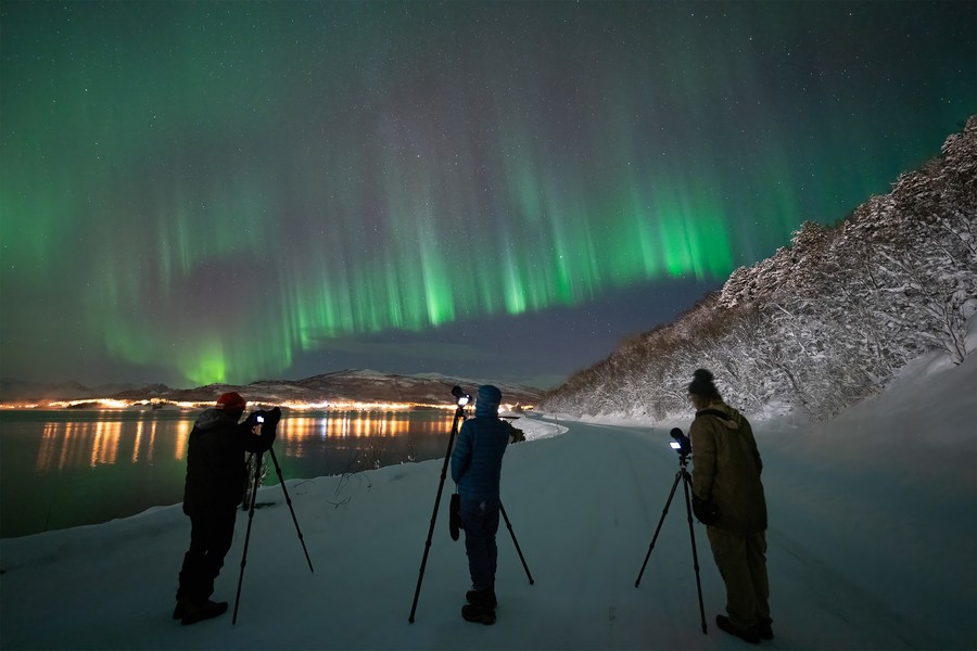Northern Lights over snowy landscape with photographers capturing the aurora.