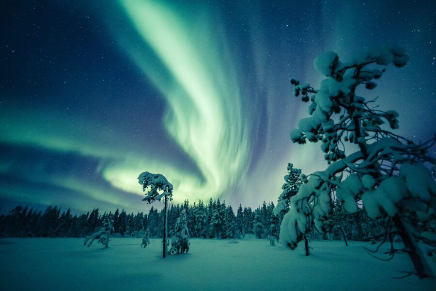 Northern lights over snowy landscape in Lapland, vibrant aurora illuminates night sky.