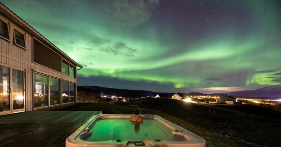 Under the shimmering aurora lights, a person enjoys a hot tub experience at the Aurora Borealis Observatory.
